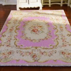A cream dollhouse miniature rug with a central pink floral medallion and golden scrollwork accents.