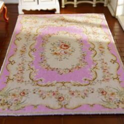A cream dollhouse miniature rug with a central pink floral medallion and golden scrollwork accents.