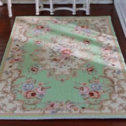 Green miniature rug with floral patterns and ornate scroll borders in pink and lavender.