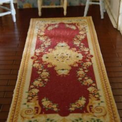 Miniature rug with a red and gold Victorian design, featuring a central medallion and surrounding floral elements.