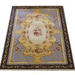 A yellow, blue and cream dollhouse miniature rug with an Aubusson-style medallion pattern and ornamental border.