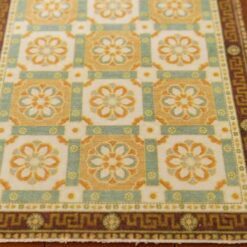 An orange and blue dollhouse miniature rug with a geometric pattern of interconnected floral motifs and Greek key border.