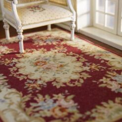 Victorian-style miniature rug in burgundy, with floral medallion and intricate scroll patterns.