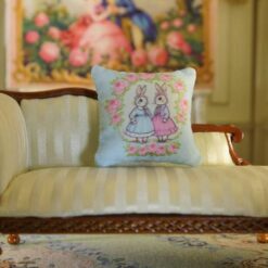 Miniature pillow design with two rabbits in blue and pink dresses surrounded by a rose wreath
