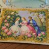 Miniature Aubusson tapestry showing a garden scene with two women and a man surrounded by roses and golden flourishes.