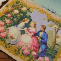 Miniature Aubusson tapestry showing a garden scene with two women and a man surrounded by roses and golden flourishes.