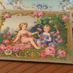 Two cherubs in a rose garden framed by ornate golden details, a miniature Aubusson tapestry.