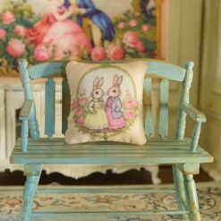 Miniature pillow with two rabbits in colorful outfits surrounded by pink roses