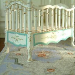 Victorian-style dollhouse crib with white frame and turquoise hand-painted details
