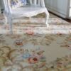 Ivory miniature rug with soft floral scroll patterns in pink, blue, and beige.