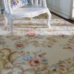 Ivory miniature rug with soft floral scroll patterns in pink, blue, and beige.