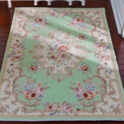 Green miniature rug with floral patterns and ornate scroll borders in pink and lavender.