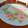 A Victorian-style round rug featuring a rose wreath medallion with pink roses and floral accents.