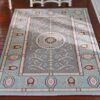 Soft blue and beige miniature rug with a floral medallion and intricate scrolling details.