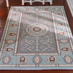Soft blue and beige miniature rug with a floral medallion and intricate scrolling details.