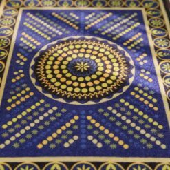 Geometric miniature rug with a spiral pattern of blue and yellow dots, bordered with floral accents.