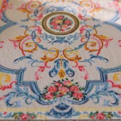 Pastel-colored miniature rug with floral accents and a central floral medallion design.