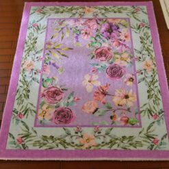 Lavender miniature rug with a pink floral border and purple blossoms with green leaves.