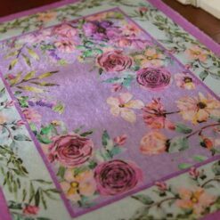 Lavender miniature rug with a pink floral border and purple blossoms with green leaves.