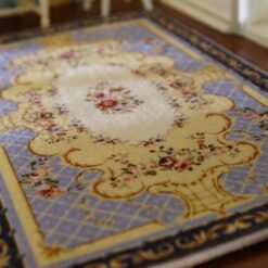 A yellow, blue and cream dollhouse miniature rug with an Aubusson-style medallion pattern and ornamental border.