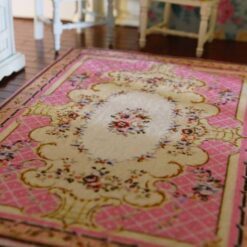 A pink, cream and burgundy dollhouse miniature rug with a central floral bouquet and scrollwork in a French country design.