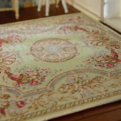 A sage green, rose and golden dollhouse miniature rug with a Persian-style floral medallion, vines and scrollwork design.