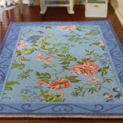 A powder blue dollhouse miniature rug with pink and blue roses, green vines, and navy scrollwork border.
