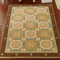 An orange and blue dollhouse miniature rug with a geometric pattern of interconnected floral motifs and Greek key border.