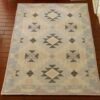 A tan and beige dollhouse miniature rug with a charcoal diamond pattern in a Southwestern Navajo style.