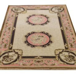 A cream dollhouse miniature rug with pink medallions, scrollwork borders, and floral accents in a French Aubusson design.