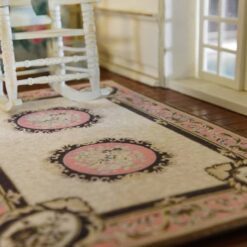 A cream dollhouse miniature rug with pink medallions, scrollwork borders, and floral accents in a French Aubusson design.