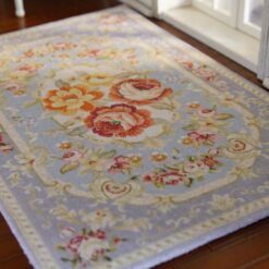 Soft blue Persian-style miniature rug with floral medallions and roses, featuring intricate scrolls and vines.