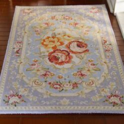 Soft blue Persian-style miniature rug with floral medallions and roses, featuring intricate scrolls and vines.