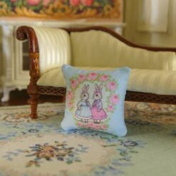 Miniature pillow design with two rabbits in blue and pink dresses surrounded by a rose wreath