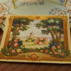 Quaint village scene framed by trees and vibrant floral borders in a miniature Aubusson tapestry.