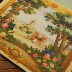Quaint village scene framed by trees and vibrant floral borders in a miniature Aubusson tapestry.