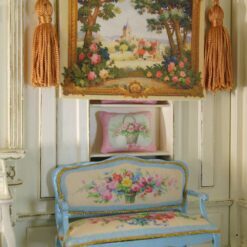 Quaint village scene framed by trees and vibrant floral borders in a miniature Aubusson tapestry.