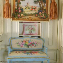 Quaint village scene framed by trees and vibrant floral borders in a miniature Aubusson tapestry.