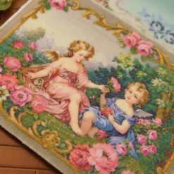 Two cherubs in a rose garden framed by ornate golden details, a miniature Aubusson tapestry.