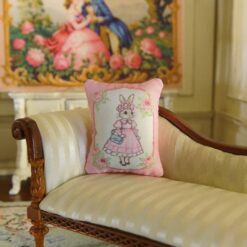 Miniature pillow with a rabbit in a pink dress and blue handbag framed by roses