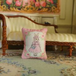 Miniature pillow with a rabbit in a pink dress and blue handbag framed by roses