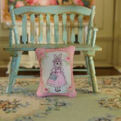 Miniature pillow with a rabbit in a pink dress and blue handbag framed by roses