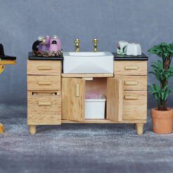 Miniature sink cabinet with black countertop and gold faucets for dollhouse bathrooms.