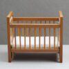 Miniature wooden baby crib with mattress for dollhouse nursery.