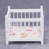 Miniature white baby crib for dollhouse nursery.
